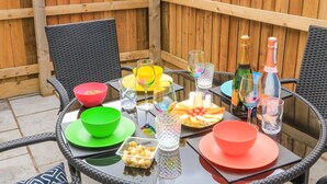 Uma mesa de vidro redonda com cadeiras, um cercado de madeira e diversos alimentos e bebidas.