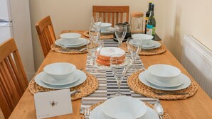 Uma mesa de jantar posta com pratos, copos e um bolo, com cadeiras ao redor.