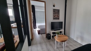 Moderni olohuone, jossa on televisio, pieni pöytä ja sohva. Seinällä on juliste ja ikkunassa sälekaihtimet.