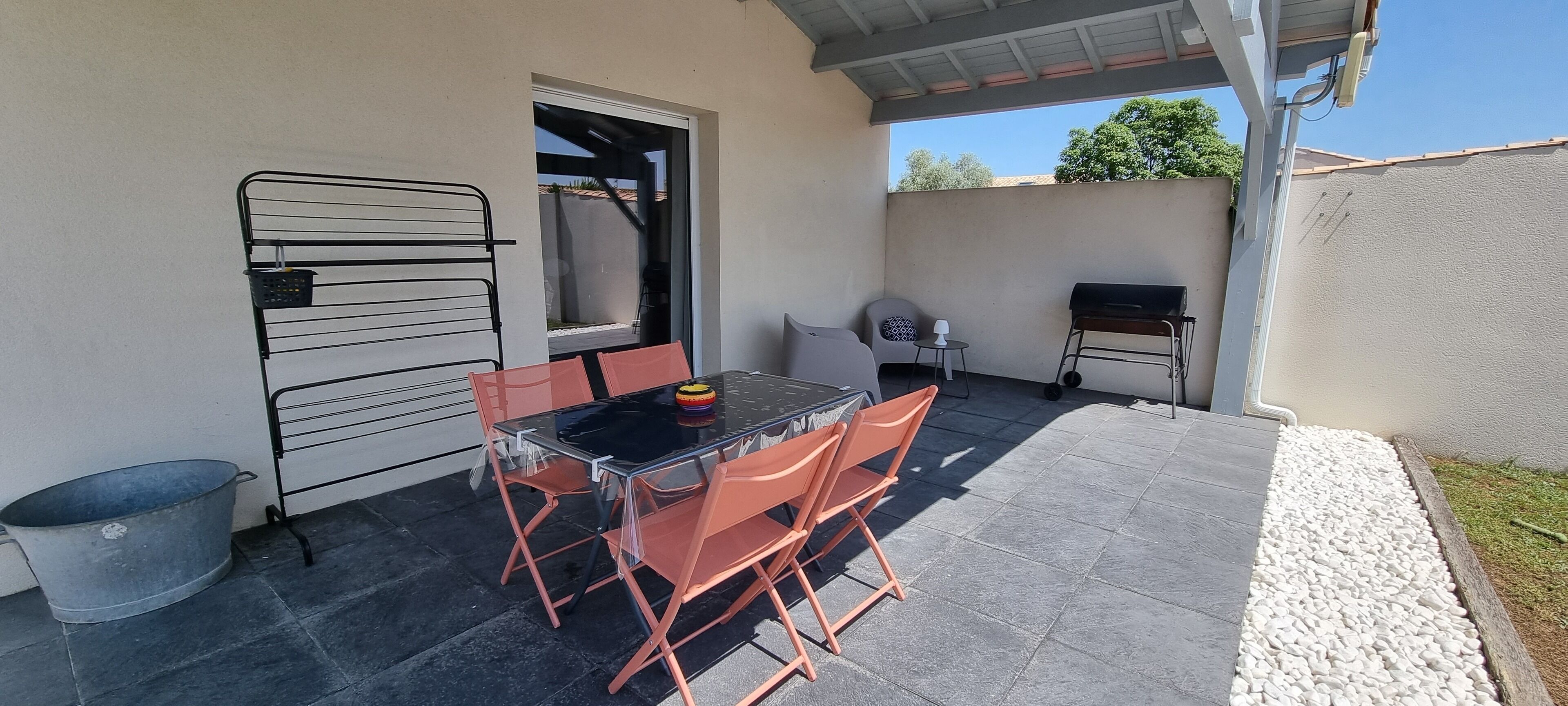 Un patio con mesa y sillas, una parrilla y un estante metálico.