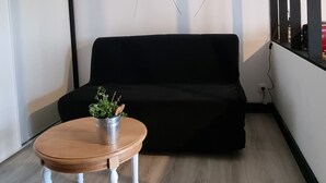 Moderni olohuone, jossa on puinen sohvapöytä, musta sohva ja seinämaalaus, jossa on kuvattuna voikukkia.
