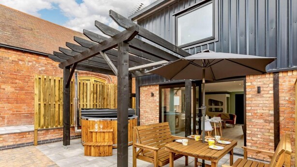 An outdoor patio with wooden furniture, a hot tub, and a pergola. - Roe Cottage - Disabled Adapted - 2 bed - hot tub (Alcester)