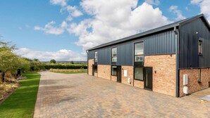 A modern building with a brick facade and large windows, featuring a paved driveway and a well-maintained lawn. - Roe Cottage - Disabled Adapted - 2 bed - hot tub (Alcester)