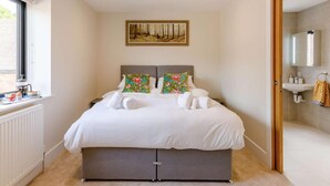 A bedroom with a bed, pillows, a painting, a window, and a bathroom visible through an open door. - Roe Cottage - Disabled Adapted - 2 bed - hot tub (Alcester)