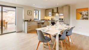 A modern kitchen with a dining area, featuring a large island, contemporary appliances, and a sliding glass door leading to an outdoor patio. - Fully Accessible-disabled Adapted-hot Tub-pets (Alcester)