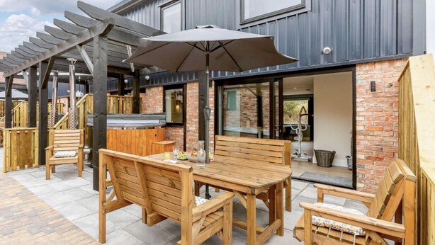 An outdoor patio with wooden furniture, a pergola, and a large umbrella. - Fully Accessible-disabled Adapted-hot Tub-pets (Alcester)