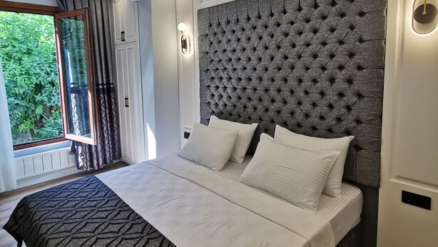 A modern bedroom with a large bed, a tufted headboard, and a view of greenery outside. - LUXX GARDEN HOTEL (Istanbul)