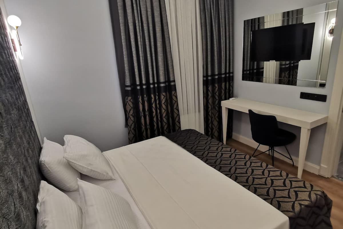 A bedroom with a bed, a desk, a chair, and a TV.