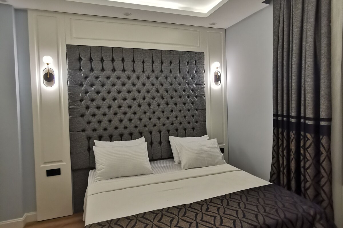 Ein modernes Schlafzimmer mit einer gepolsterten Kopfteil, einem großen Bett mit gemusterten Betttextilien und zwei Wandleuchten.