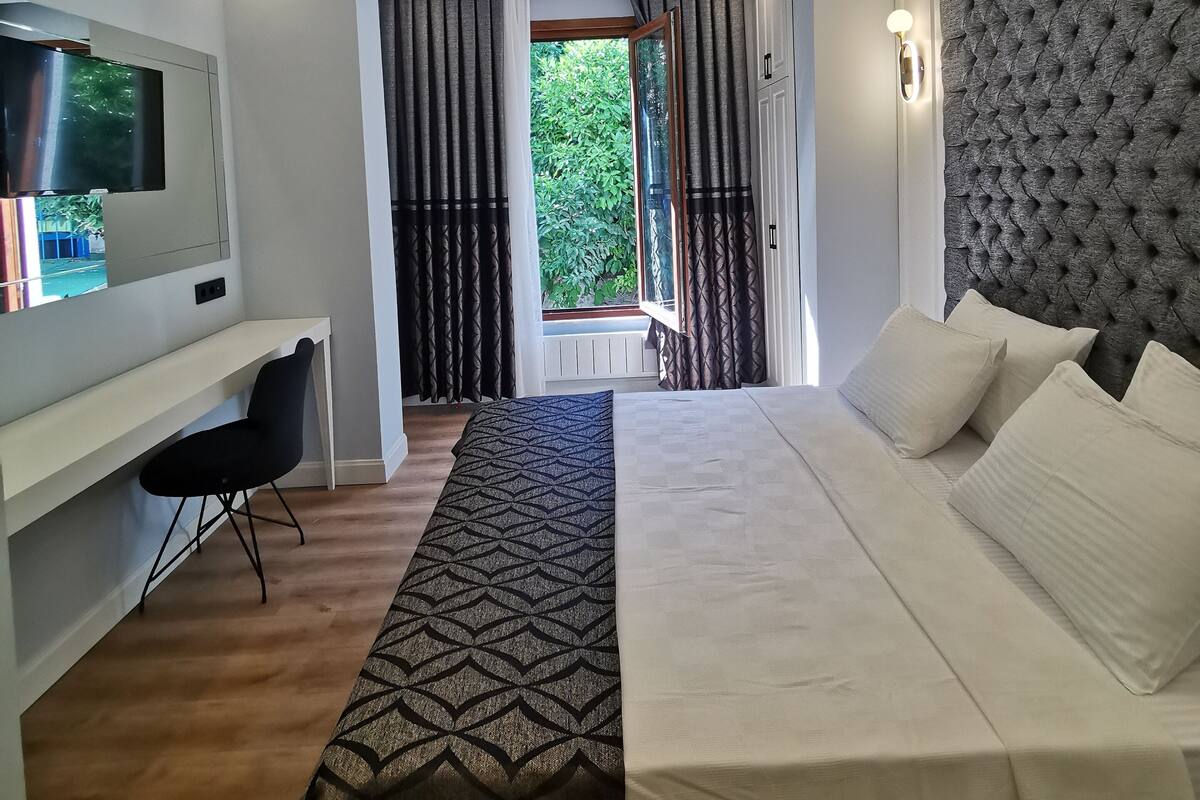 A modern bedroom with a bed, a TV, a desk, and a window with curtains.