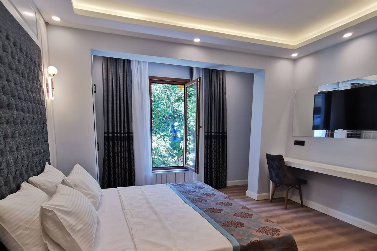 A modern bedroom with a large bed, a desk, a TV, and a window with curtains.