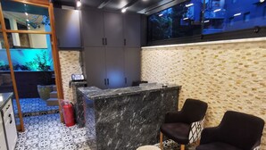 A modern kitchen with a marble countertop, dark cabinets, and a view of the city at night. There are two wooden stools and two black chairs with a geometric pattern. - LUXX GARDEN HOTEL (Istanbul)