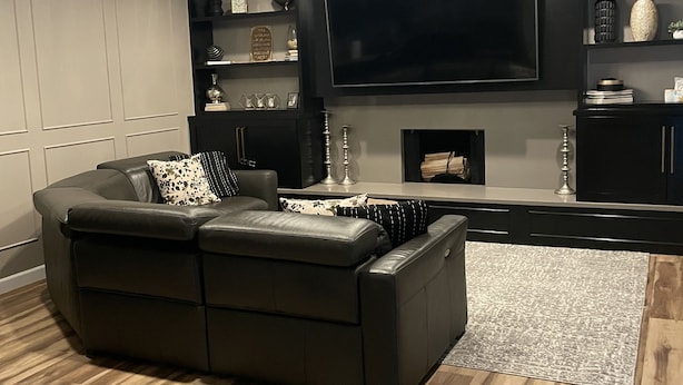 Un salon moderne avec un canapé d’angle, un téléviseur à écran plat, un lustre et une cheminée.