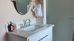 Une salle de bain avec un meuble-lavabo blanc, un miroir, un évier et une douche.
