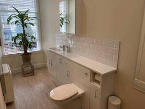 Ein modernes Badezimmer mit Toilette, Waschbecken und Schränken. Auf einem kleinen Tisch neben dem Fenster steht ein Blumentopf.