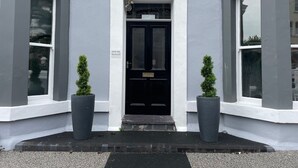 L’entrée d’un immeuble avec une porte noire, deux plantes en pot et une enseigne indiquant « CRIME RISE APARTMENTS ».