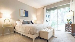 A bedroom with a bed, bedside tables, a bench, and a view of the outdoors.