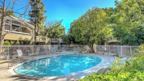 A swimming pool surrounded by a fence, with trees and a building in the background.