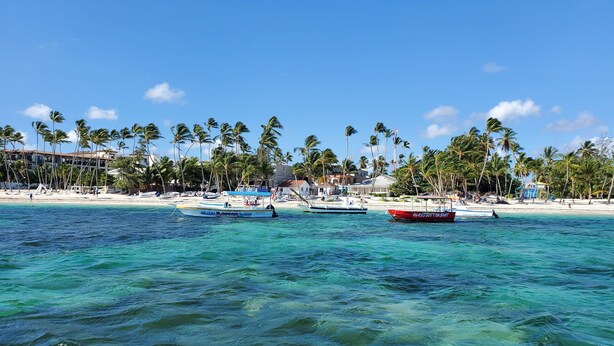 Una playa con aguas turquesas cristalinas, palmeras y barcos.