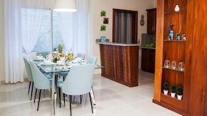 Un comedor con una mesa y sillas de vidrio, un aparador de madera con objetos decorativos, y una cocina al fondo.