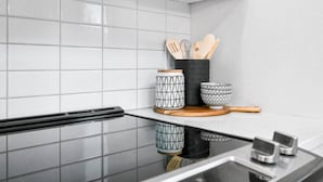 A kitchen with white tiled backsplash, a black countertop, and a wooden cutting board. There are two patterned bowls and a black container with wooden utensils. - Hideaways| Mins to Lake| King Bed |Dbl Garage| AC (Invermere)