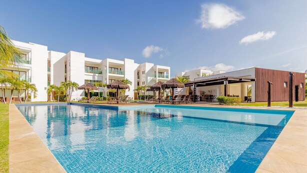 Piscina con sillones de descanso y sombrillas, rodeada de edificios modernos con balcones.