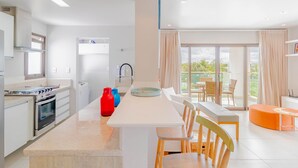 Una cocina moderna con una isla central, un área de comedor con mesa y sillas, y un balcón con vistas.