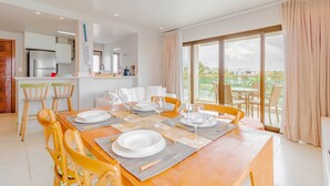 Un comedor moderno con una mesa de madera dispuesta para cuatro, una cocina al fondo y un balcón con vistas.