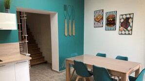 Eine moderne Küche mit Holzarbeitsplatte und weißen Schränken, ein Essbereich mit Holztisch und türkisfarbenen Stühlen sowie eine Treppe zu einer oberen Ebene.