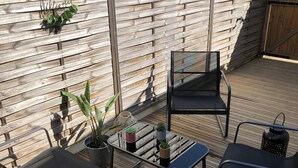 Eine Holzterrasse mit einem Metalltisch und zwei Stühlen, umgeben von Topfpflanzen und einer dekorativen Leuchte.