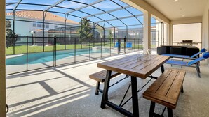 Ein überdachter Außenbereich mit Pool, Holztischen und -stühlen sowie einem Grill.