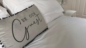 Ein Bett mit weißer Bettwäsche und einem Kissen mit dem Aufdruck "BE OUR Guest".