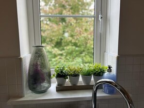 Una ventana con marco blanco, un florero de cristal y tres plantas en macetas sobre el alféizar.