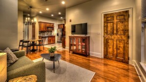 A spacious living room with a wooden floor, a dining area with a table and chairs, a kitchen with wooden cabinets, and a large wooden door. - Perch 3 - Luxury Condo | Downtown Location | Modern and Contemporary (Blue Ridge)