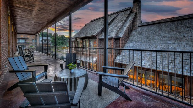 A covered outdoor seating area with chairs and a table, overlooking a building with a stone facade and a wooden roof. - Perch 3 - Luxury Condo | Downtown Location | Modern and Contemporary (Blue Ridge)