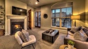A living room with a fireplace, a leather sofa, a coffee table, and a large window with blinds. - Perch 3 - Luxury Condo | Downtown Location | Modern and Contemporary (Blue Ridge)