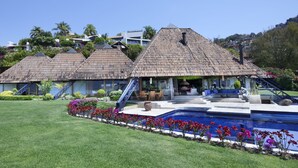Un complexe hôtelier comprenant plusieurs bâtiments à toits de chaume, une piscine et des jardins bien entretenus.