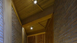 Un couloir étroit aux poutres en bois et aux murs en briques, qui mène à une porte en bois au bout.