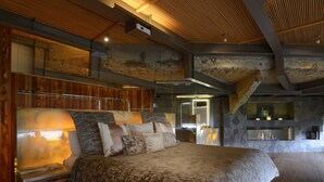 Une chambre spacieuse avec un grand lit, une tête de lit en bois et une cheminée en pierre.