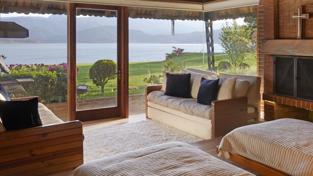 Une chambre avec une grande fenêtre, des poutres apparentes en bois au plafond, une cheminée et une vue sur la mer.