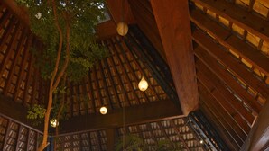 Un vaste espace intérieur doté d’un haut plafond, de poutres en bois et d’une grande table en verre entourée de chaises.