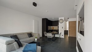 A modern living room with a grey sofa, a coffee table, and a dining area with chairs and a table. - Modern apartment with garage box and free wifi (Willebroek)