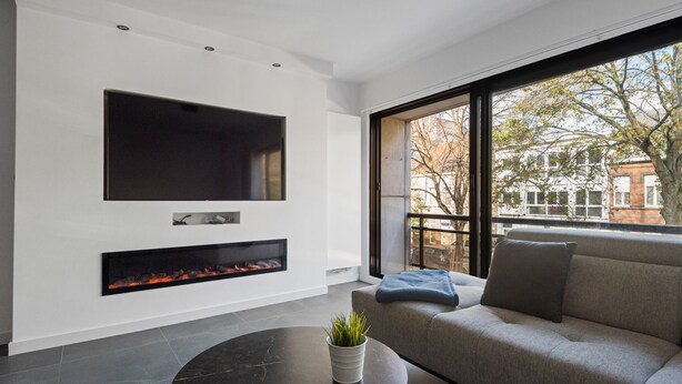 A modern living room with a flat-screen TV, a fireplace, a sofa, and a balcony with a view of buildings. - Modern apartment with garage box and free wifi (Willebroek)