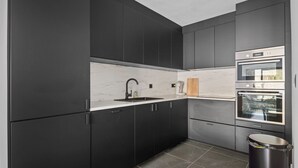 A modern kitchen with dark cabinetry, a marble countertop, and stainless steel appliances. - Modern apartment with garage box and free wifi (Willebroek)