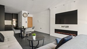 A modern living room with a grey sofa, a dining area with a table and chairs, a kitchen with an oven, and a fireplace. - Modern apartment with garage box and free wifi (Willebroek)