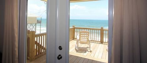 A sliding glass door leading to a wooden deck with a view of the ocean.