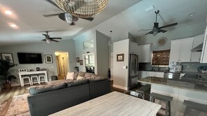 Una sala de estar moderna con un amplio sofá modular, una mesa de comedor y una cocina con armarios blancos y un refrigerador de acero inoxidable.