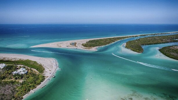 Vista aérea de una zona costera con aguas turquesas cristalinas, una playa de arena y una pequeña isla con vegetación densa.