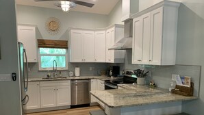 Una cocina moderna con armarios blancos, lavavajillas de acero inoxidable, horno empotrado y una isla grande con taburetes de bar.