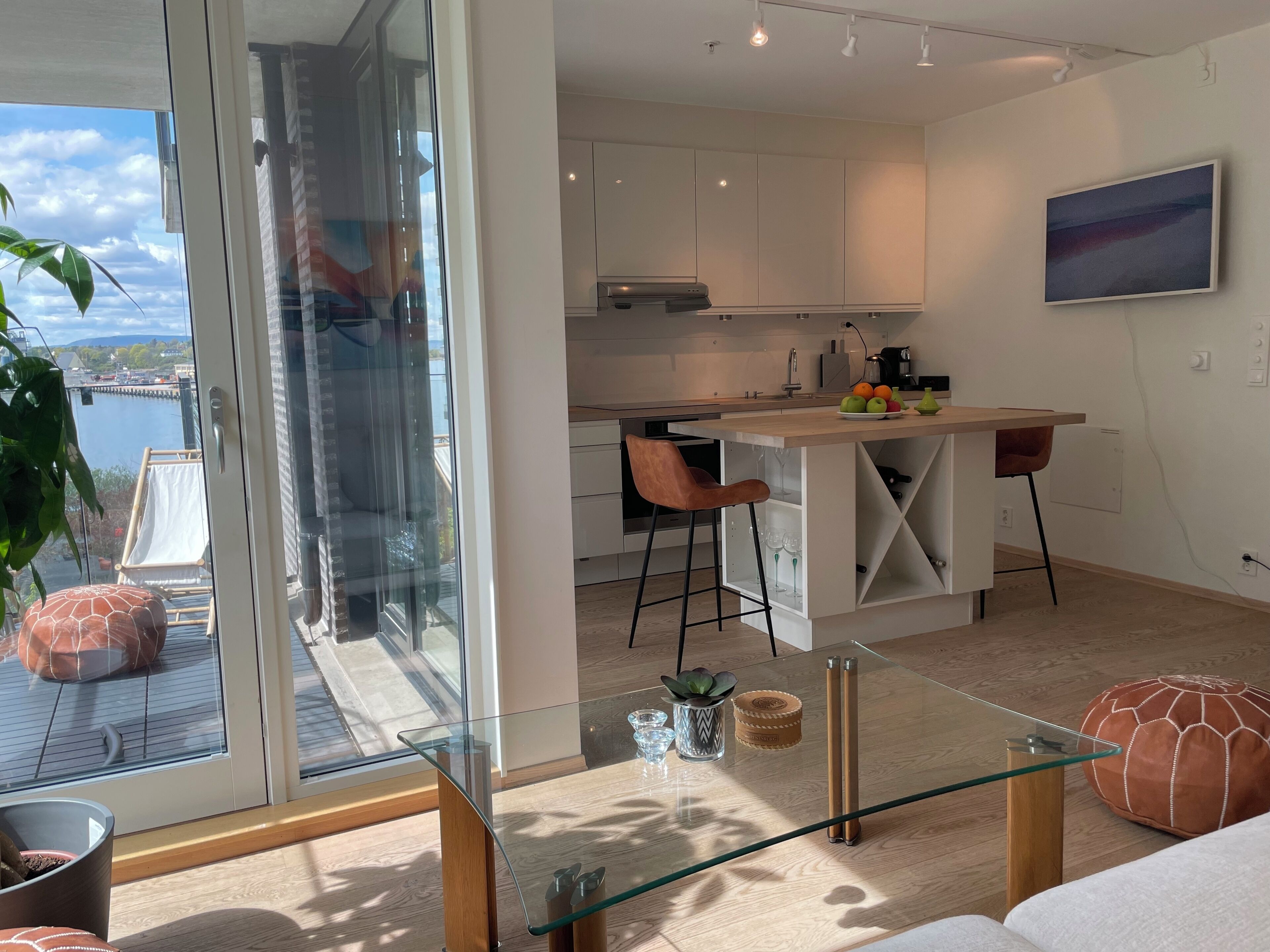 A modern kitchen with a central island, a dining area with two chairs, and a large window overlooking a body of water.